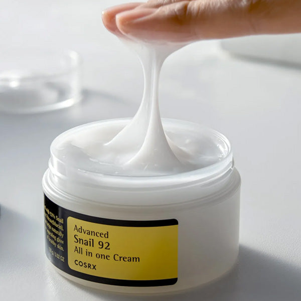 Hand scooping thick white face cream from Advanced Snail 92 All in One Cream jar by COSRX