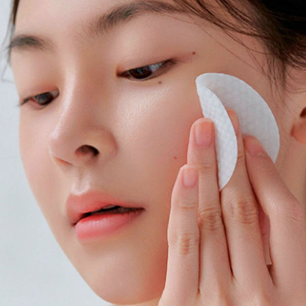 Woman using toner pad on face for skincare routine, close-up of glowing skin